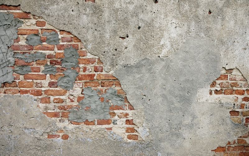 A weathered brick wall with patches of grey plaster and exposed red bricks